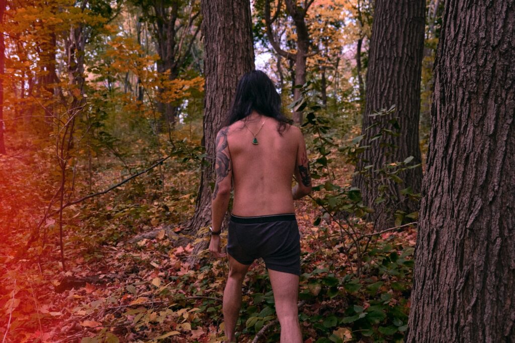topless man in black shorts standing on forest during daytime